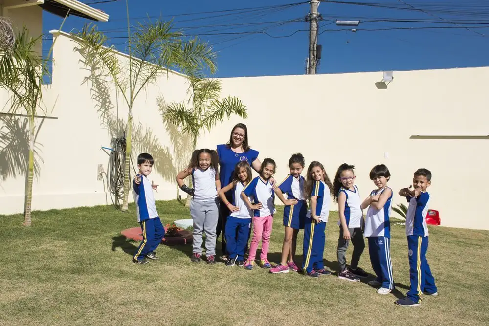 Alunos uniformizados posando com professora no pátio do Colégio Barcelos
